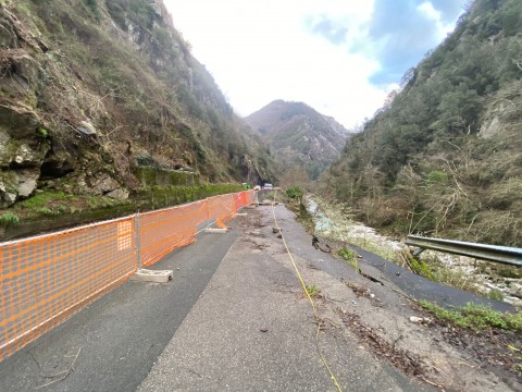 Nella foto in primo piano porzione di carreggiata con a destra il movimento franoso sul lato del fiume e a sinistra la rete carancione che delimita il cantiere