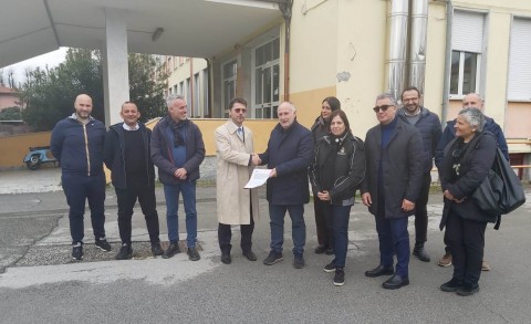 Nella foto al centro il presidente Lorenzetti stringe la mano all'ingegner Belloni, foto di gruppo con le persone indicate nel comunicato, sullo sfondo l'istituto che verrà demolito