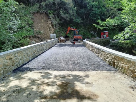 In primo piano il ponte con la porzione di strada e prima stesura asfalto, ai lati le nuove spallette realizzate in sassi a a vista