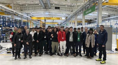 Foto di gruppo degli studenti al centro del capannone sotto una campata con la scritta Aero Alliance