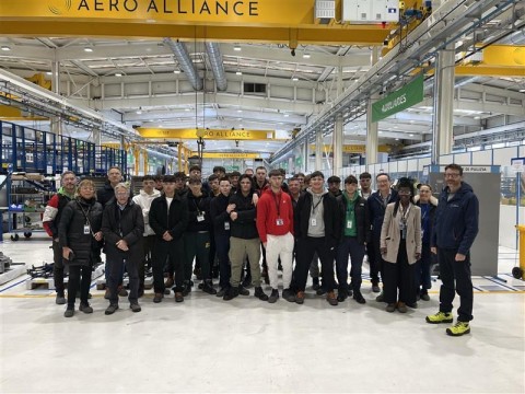 Foto di gruppo degli studenti al centro del capannone sotto una campata con la scritta Aero Alliance