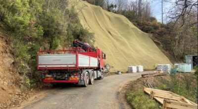 Nela foto in primo piano un camion lungo la strada, in secondopiano la scarpata con alcuni teli in tesuto naturale stesi lungo il fianco della stessa
