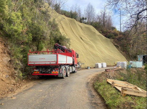Nela foto in primo piano un camion lungo la strada, in secondopiano la scarpata con alcuni teli in tesuto naturale stesi lungo il fianco della stessa